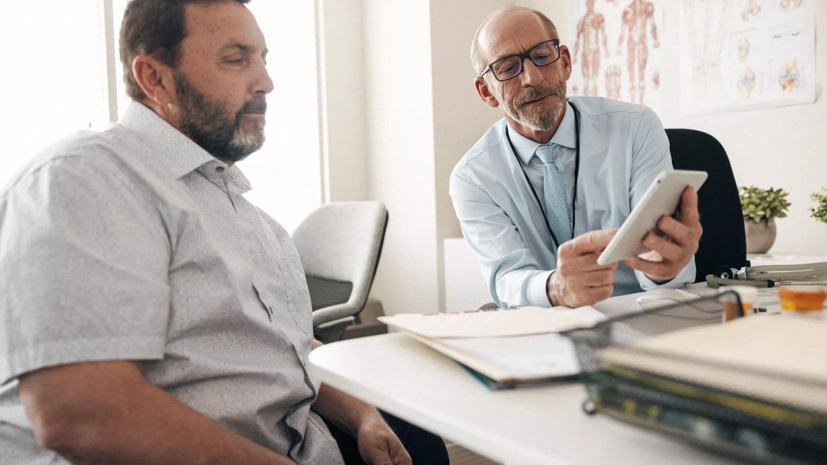 Two men sitting at a table looking at a tablet.