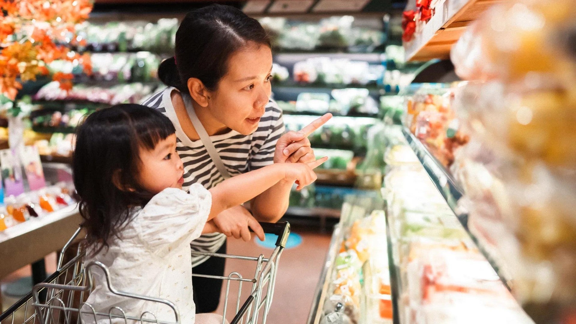 Mother and her toddler-aged daughter shop the produce section of the grocery store.