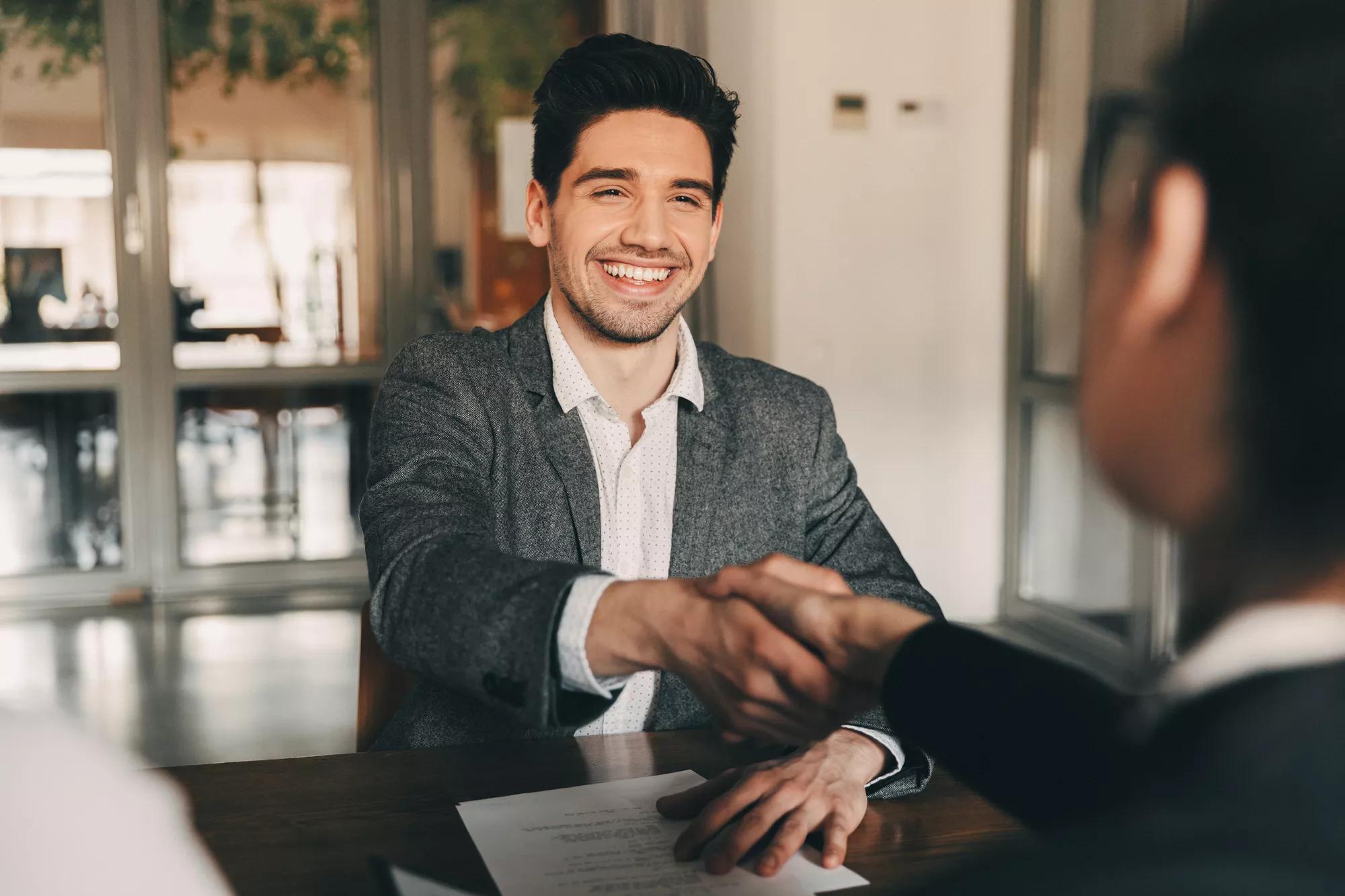 Young man shaking hands across a desk. 