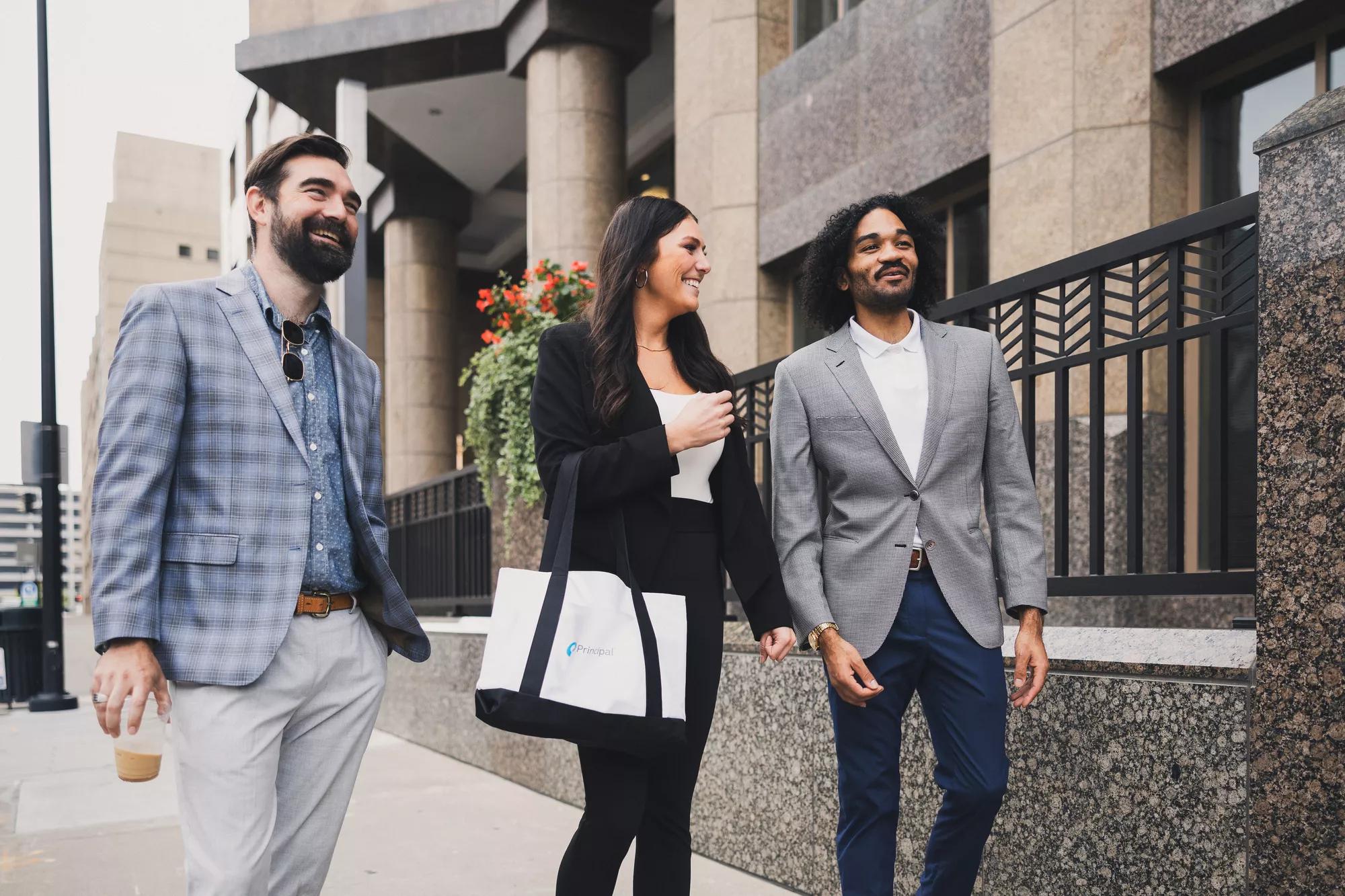 Three people walking outside of a Principal building.