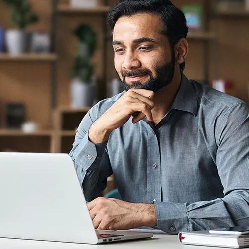 Bearded Indian business man watching online webinar on laptop computer.