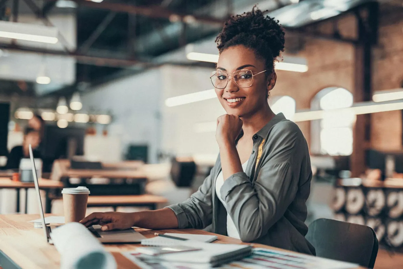 A smiling woman at her desk with a cup of coffee