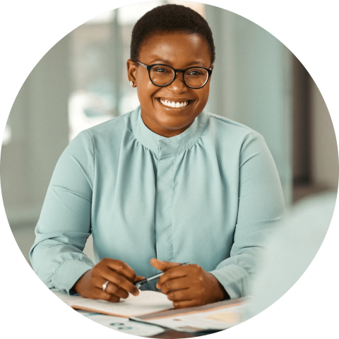 Woman in glasses holding a pen smiling.