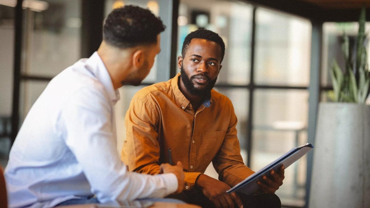 Two men talking in a small office setting.