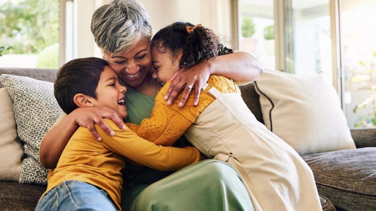 A grandmother hugging her grandchildren indoors.