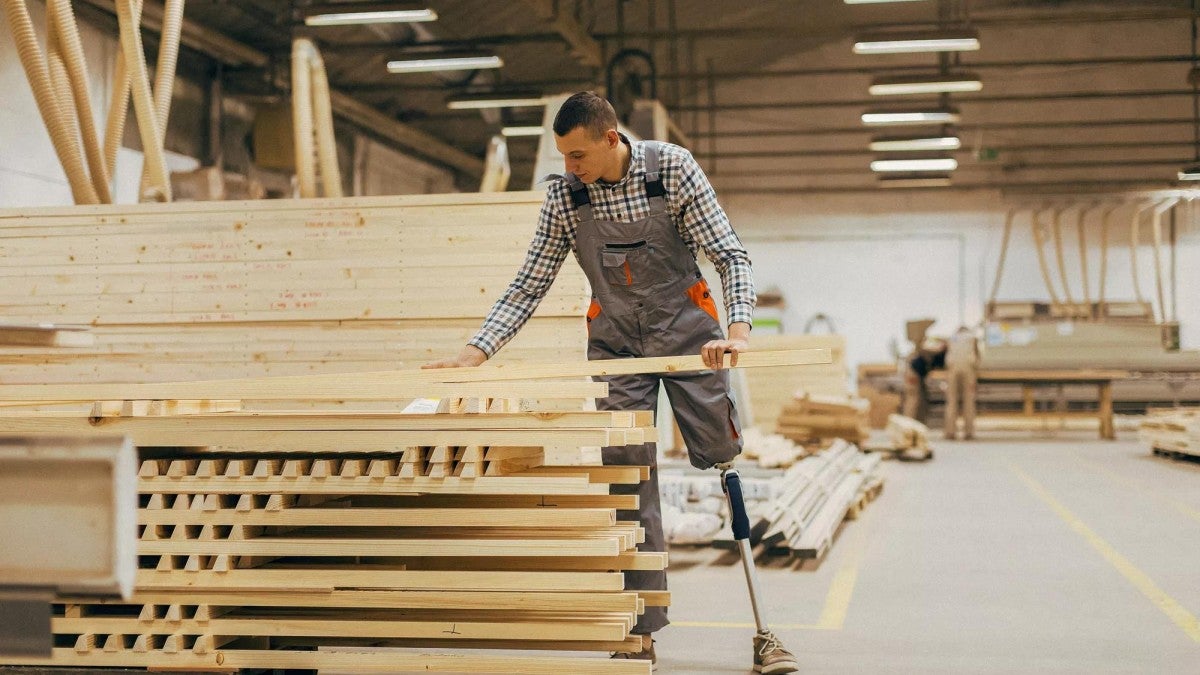 A man with a prosthetic leg moving lumber in a ware house.