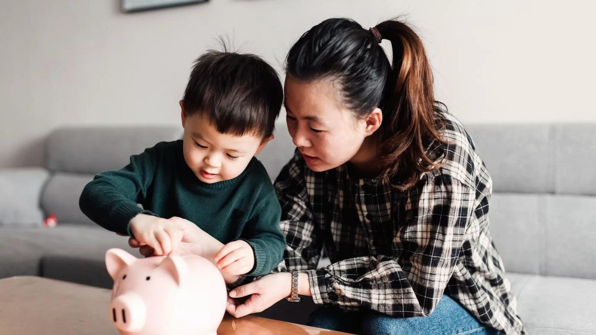 A mother and her child putting coins in a piggy bank.