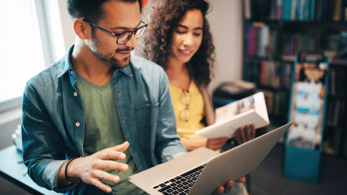 Two college students looking at a laptop in the school library.