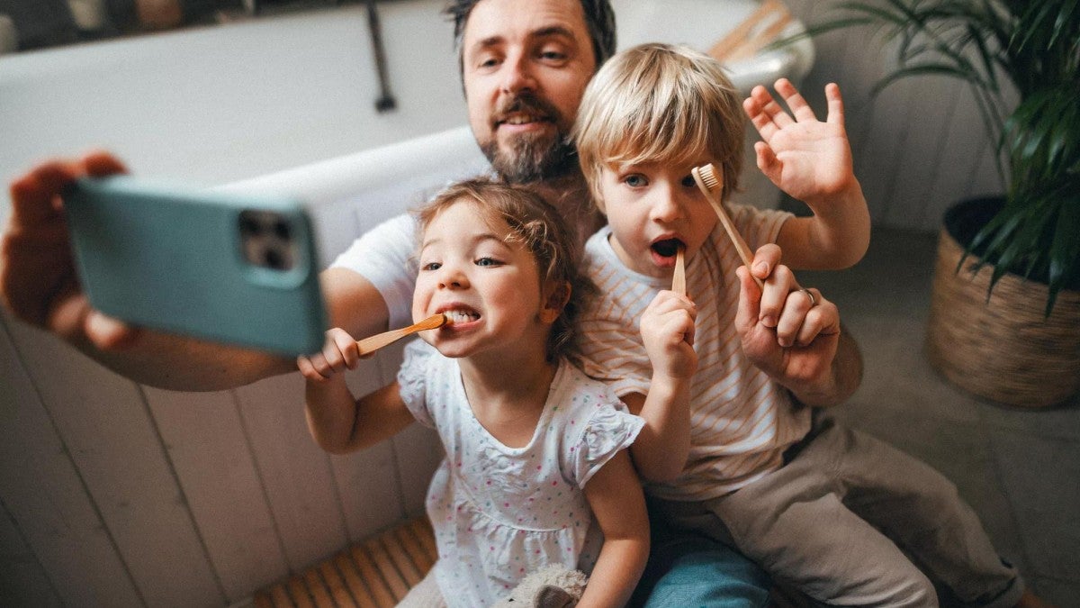 A man taking a selfie with his children while they brush their teeth.