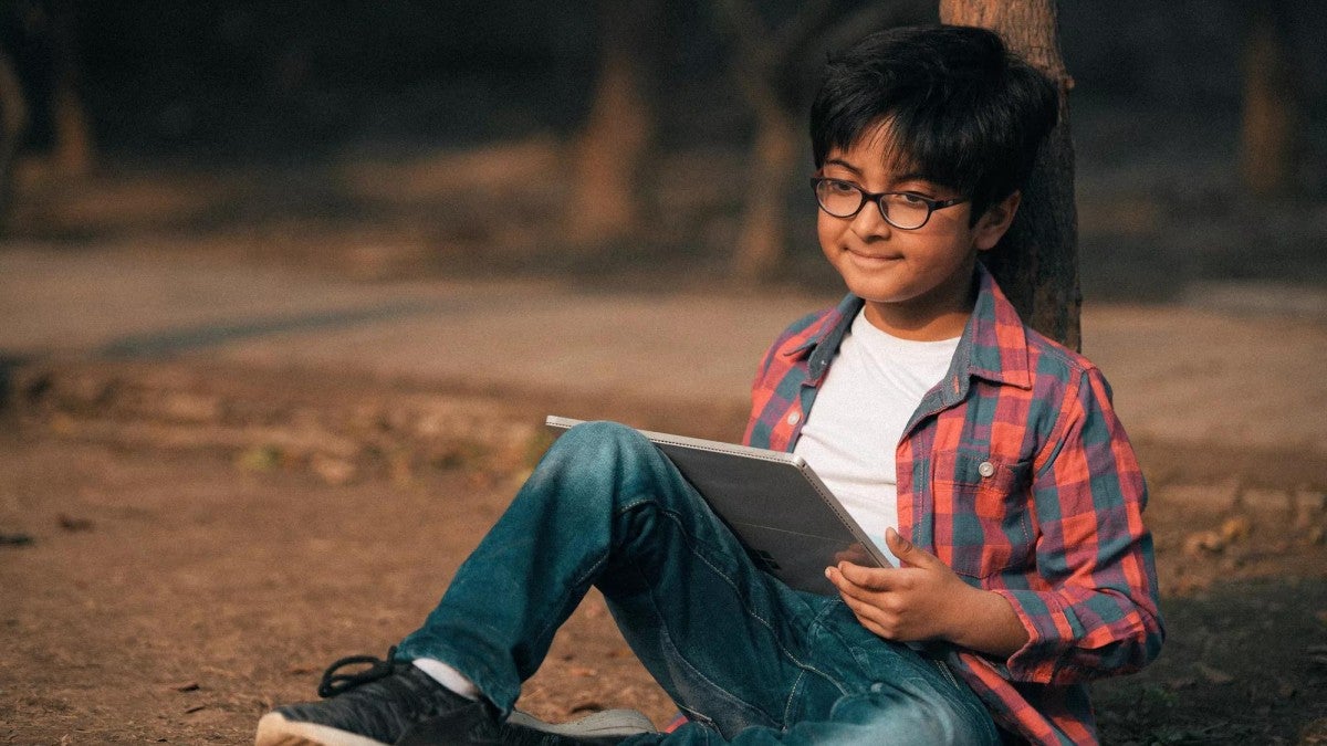 A boy sitting on the ground with a sketch pad.