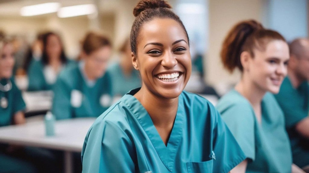  Image of a nurse smiling within a classroom of other nurses. 