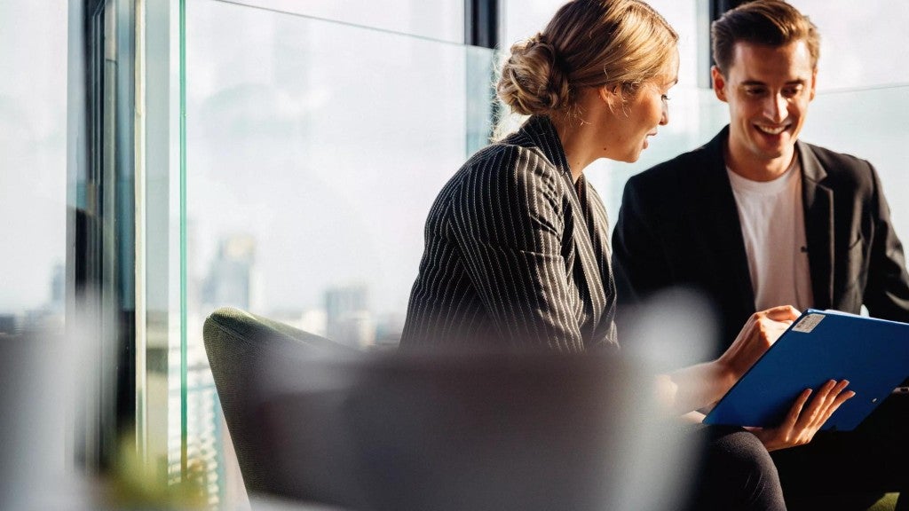 A man and woman look at a laptop in an office setting.