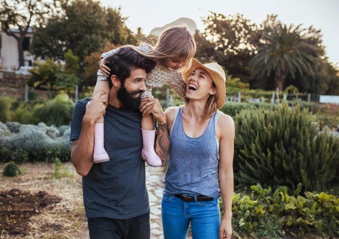 Millennial man and woman walking in nature with child on man's shoulders.