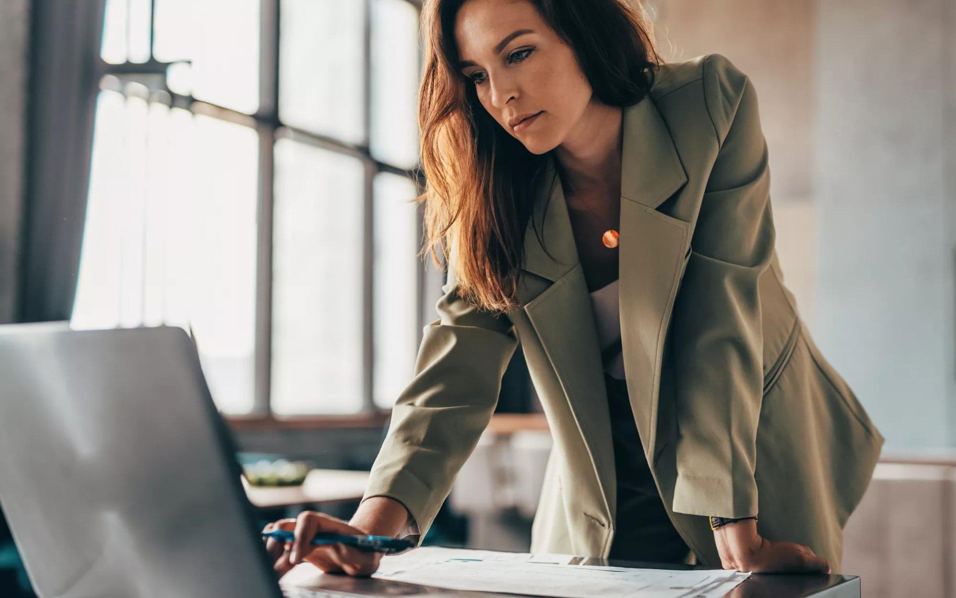 Woman standing, working on a laptop in an office setting.