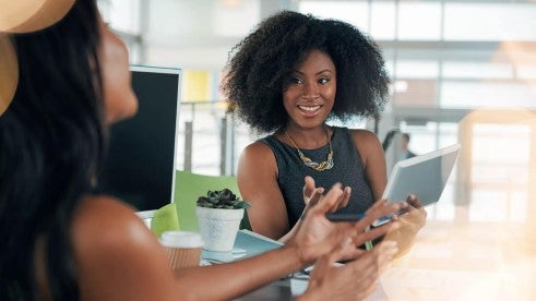 A happy, smiling person checks their tablet while working with a colleague.