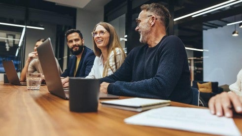 An employee is recognized during a team meeting while the rest of the team at the table nods approvingly in the background.