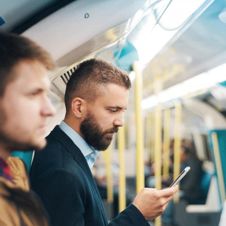 Hombre en un tren subterráneo mirando su teléfono móvil, revisando el saldo de su cuenta en la aplicación móvil.